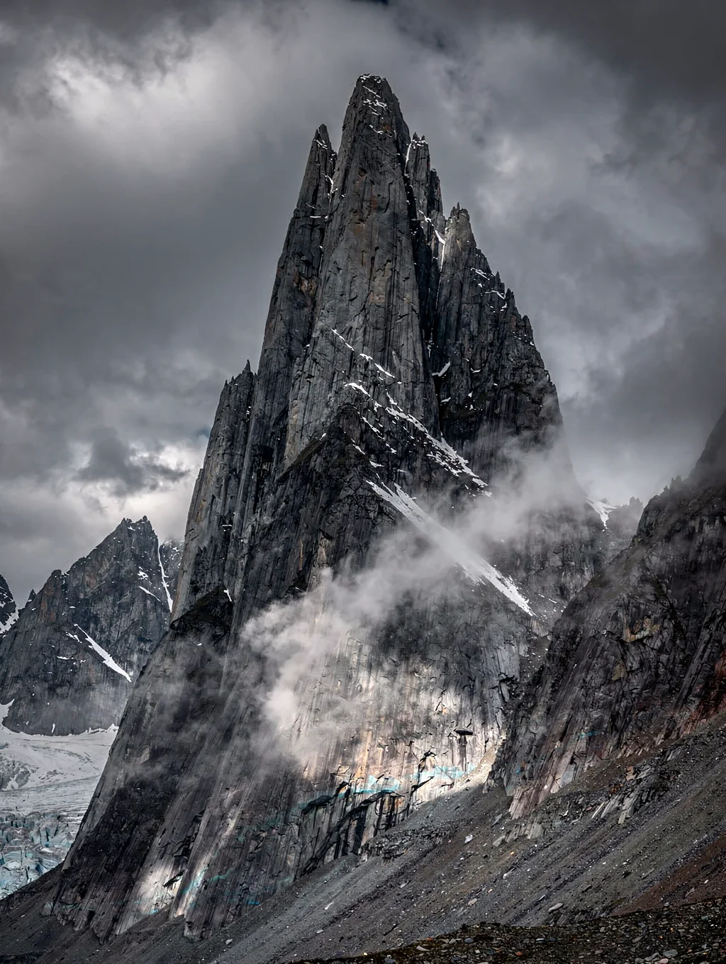 Granite needle of Cerro Torre shrouded in alpine storm clouds with golden sunrise rim